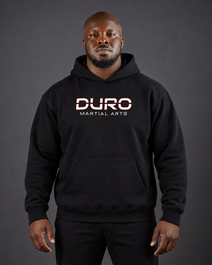 Coach Jullien Shelby modeling the black DURO Martial Arts Heavyweight Hoodie — AI-assisted studio image